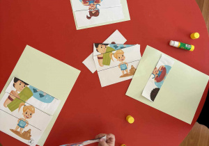 Przedszkolaki podczas układania puzzli i przyklejania ich na kartkę.