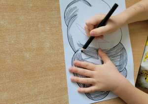 Dziecko koloruje chmurkę czarną kredką.