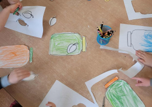 Dzieci wycinają szablon śliwki z papieru i przyklejają je na słoik.