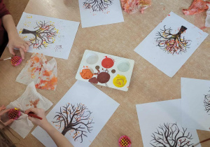 Dzieci wykonują pracę plastyczną pt.: "Jesienne drzewo" techniką stemplowania.