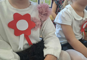 Dziewczynki w białych bluzkach z przypiętymi kotylionami w barwach narodowych.