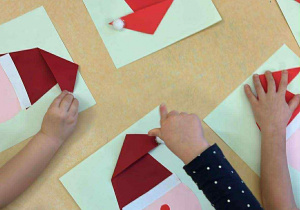 Dzieci podczas przyklejania twarzy i czapki Mikołaja.