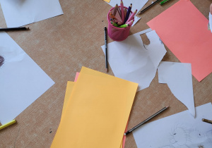 Dzieci wycianją jeże z papieru i naklejają na kolorową kartkę.