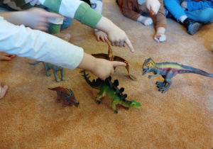 Dzieci oglądają figurki dinozaurów.