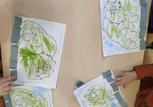 Dzieci kolorują kolorowankę przedstawiającą dinozaura.