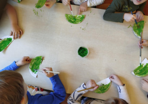 Dzieci malują zieloną farbą papierowy talerzyk.