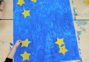 Dzieci przyklejają papierowe gwiazdki na niebieski karton.