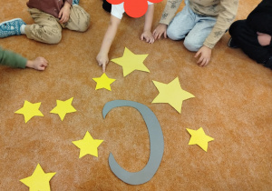 Dzieci liczą papierowe gwiazdy rozłożone na dywanie.