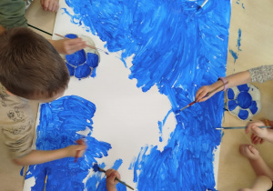 Dzieci maluja karton niebieską farbą.