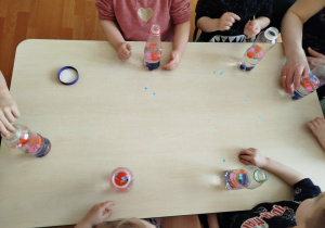 Dzieci wrzucają kolorowe elementy do butelek.