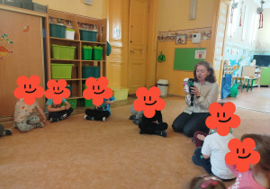 Dzieci siedzą na dywanie i słuchają pani prowadzącej warsztaty.