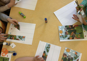 Przedszkolaki podczas wycinania i przyklejania puzzli.